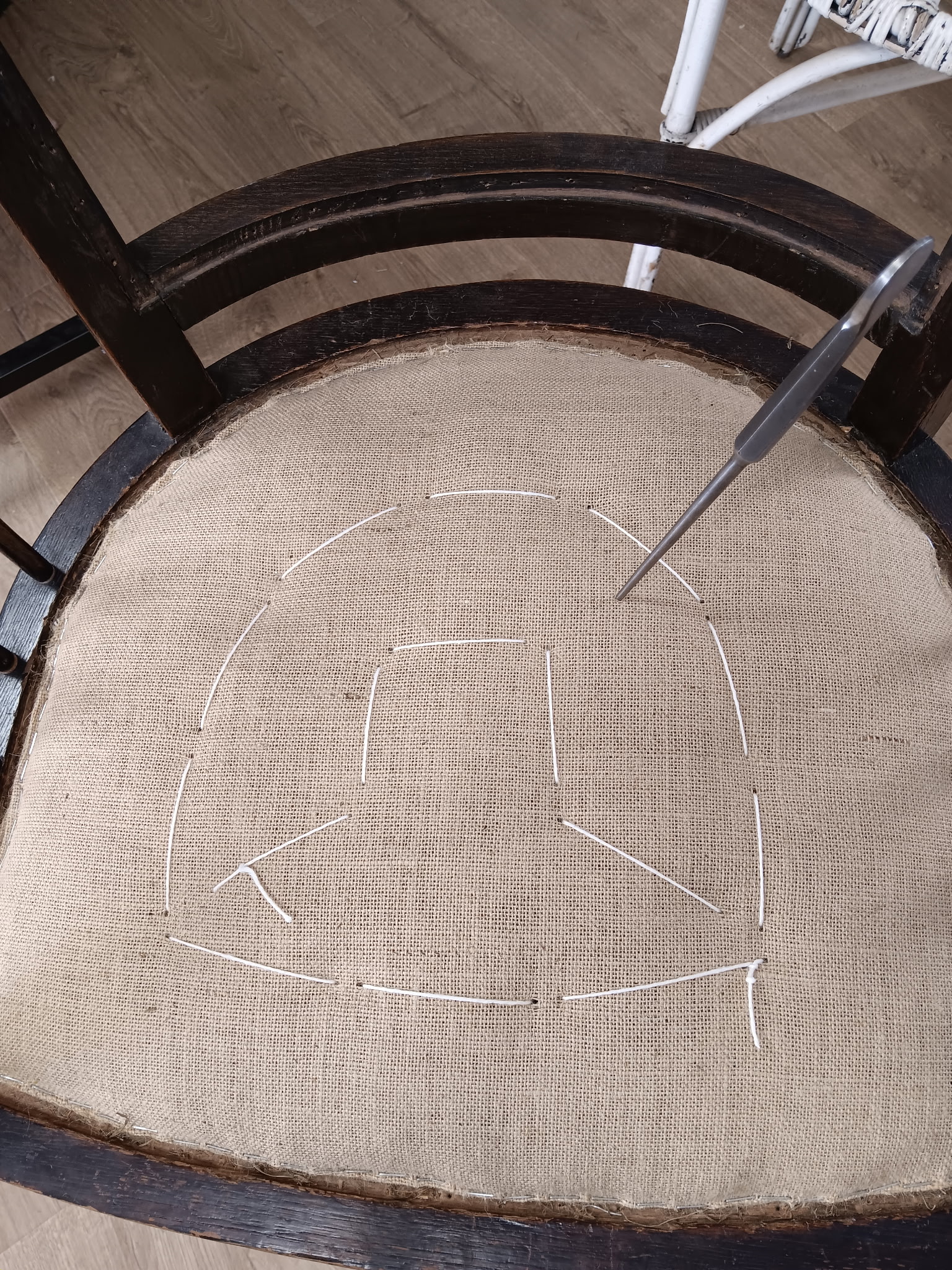 Un carrelet traverse la toile de jute de l’assise pour réaliser les points de fond à la main