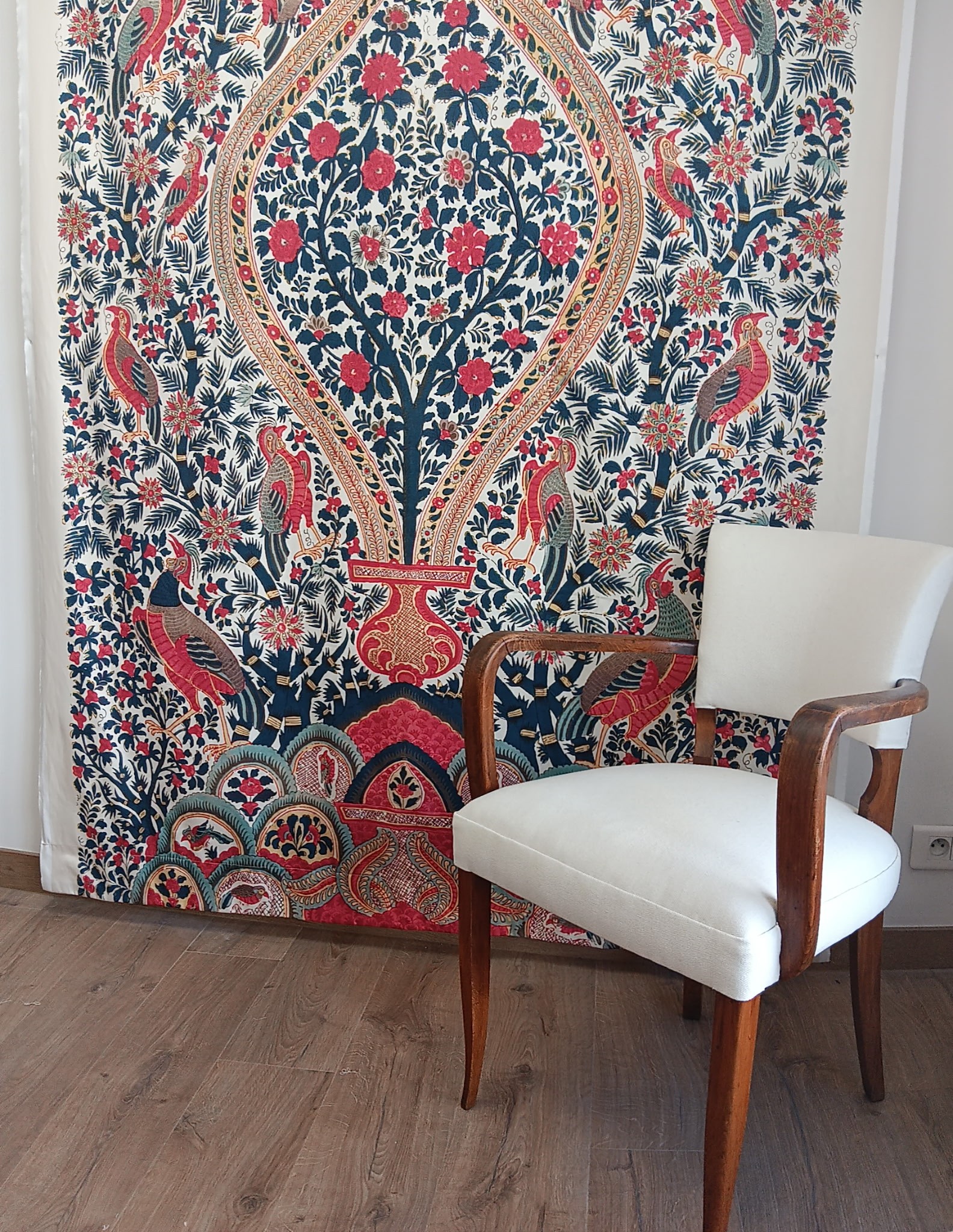 Fauteuil bridge habillé d’un tissu clair devant une étoffe aux motifs floraux et oiseaux colorés